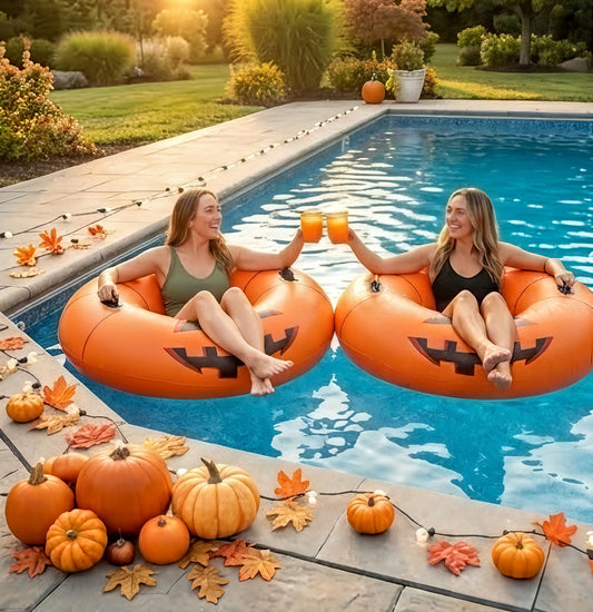 Two women on pumpkin-shaped inner tubes in a pool with Halloween decorations.